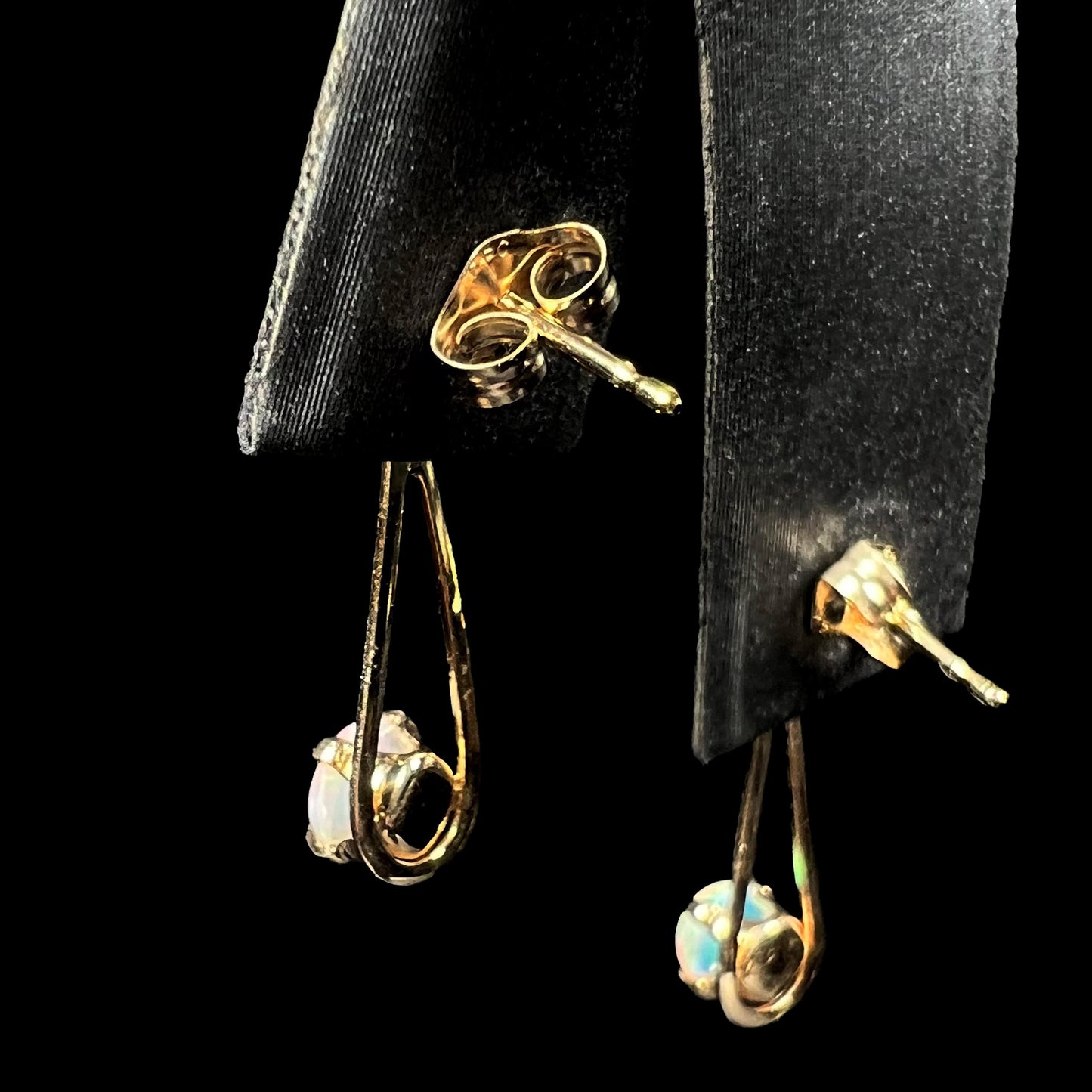 Back side of pair of gold opal dangle earrings on earring display, focused on the posts and butterfly backs.