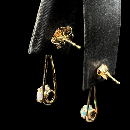 Back side of pair of gold opal dangle earrings on earring display, focused on the posts and butterfly backs.
