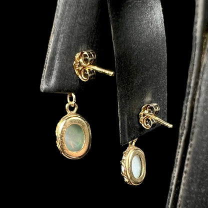Back side of a pair of yellow gold Australian light opal dangle earrings with pushbacks, shown on an earring display.