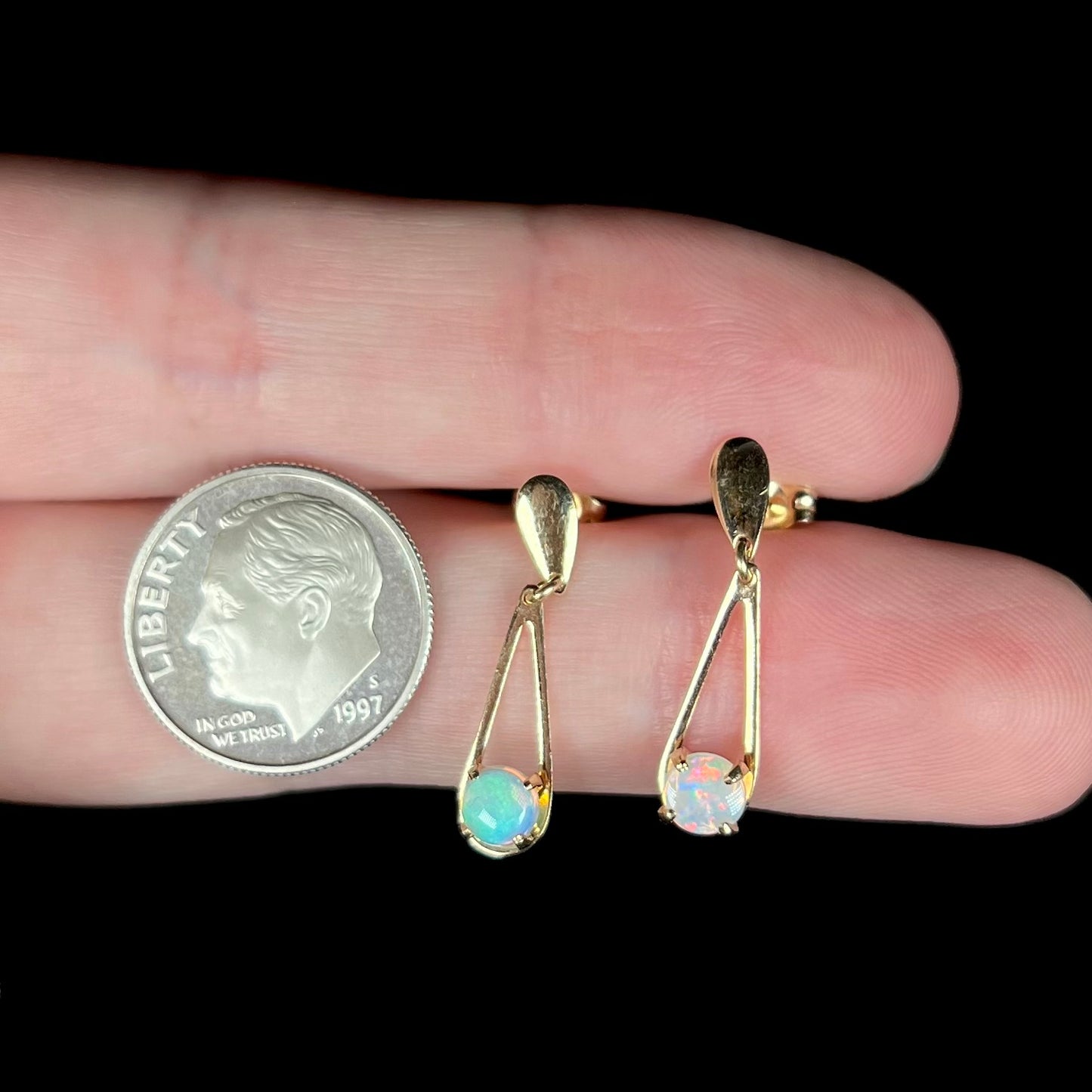 Pair of gold round crystal opal dangle earrings held between two fingers next to a US dime coin.