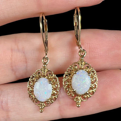 A pair of vintage yellow gold Australian light opal dangle earrings shown close-up in a hand from the front.