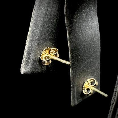 The back of opal stud earrings, showing 14k gold friction backs and posts against a black background. Earrings are not visible.