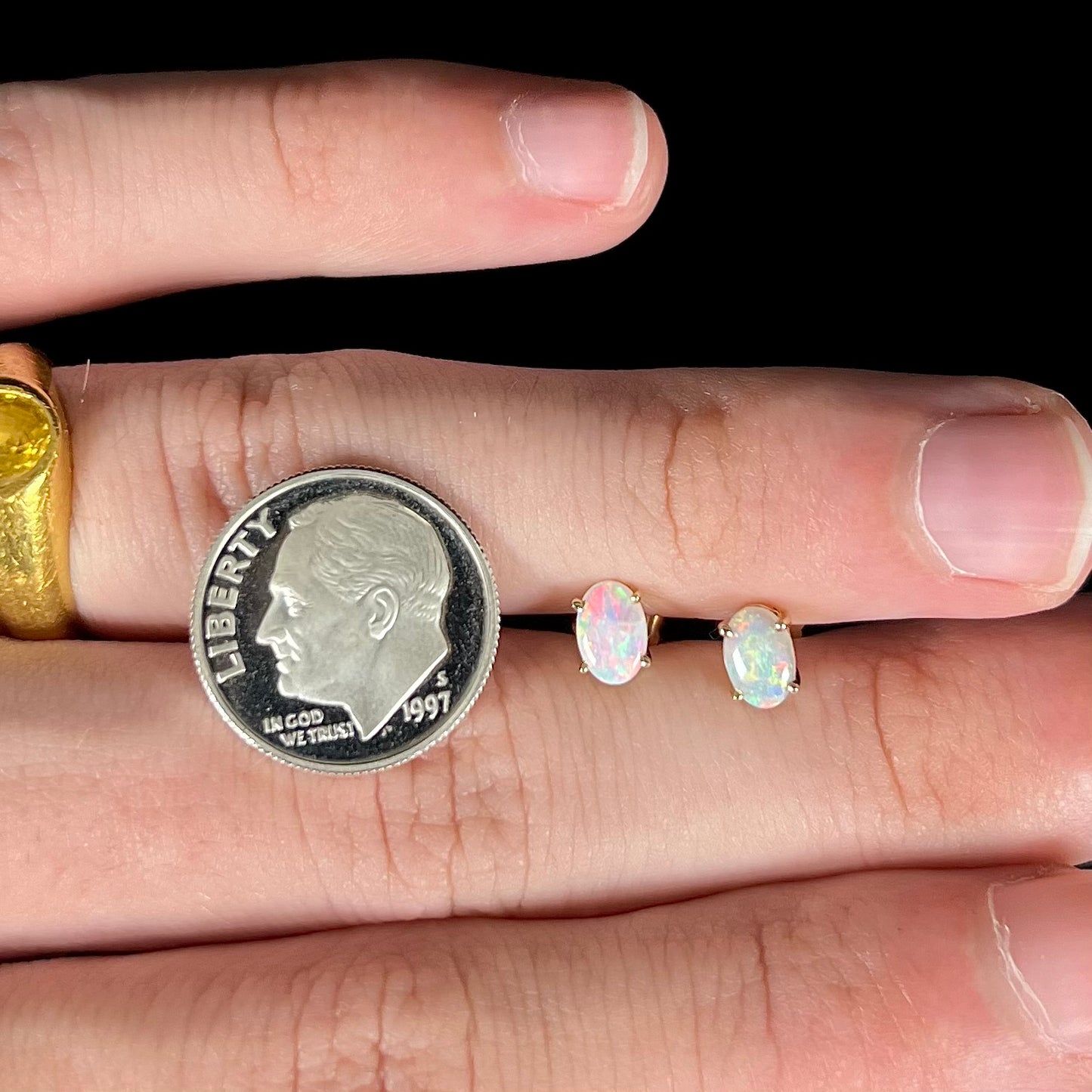 Gold opal earrings resting on fingers with a dime for scale.