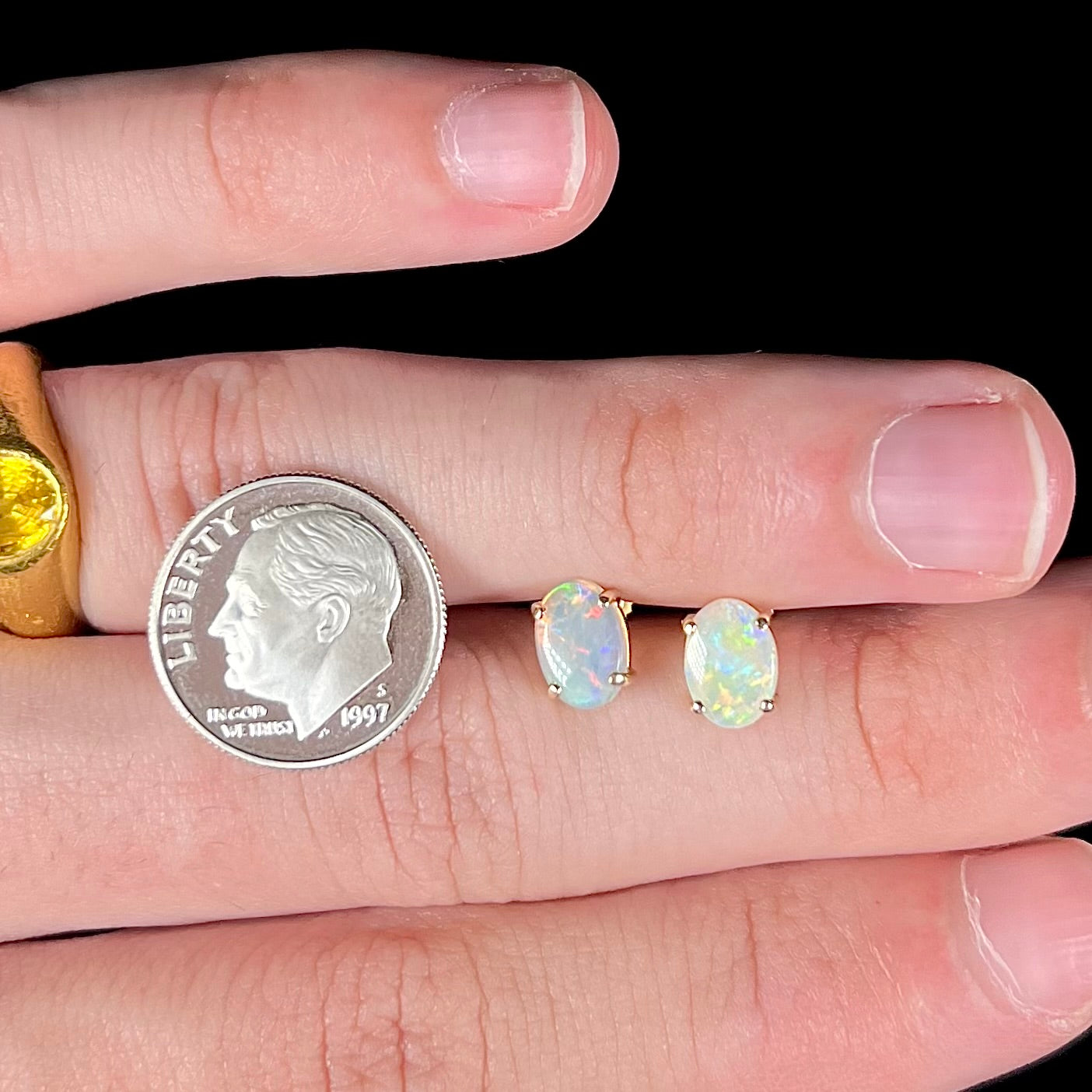 Gold opal earrings resting on fingers with a dime for scale.