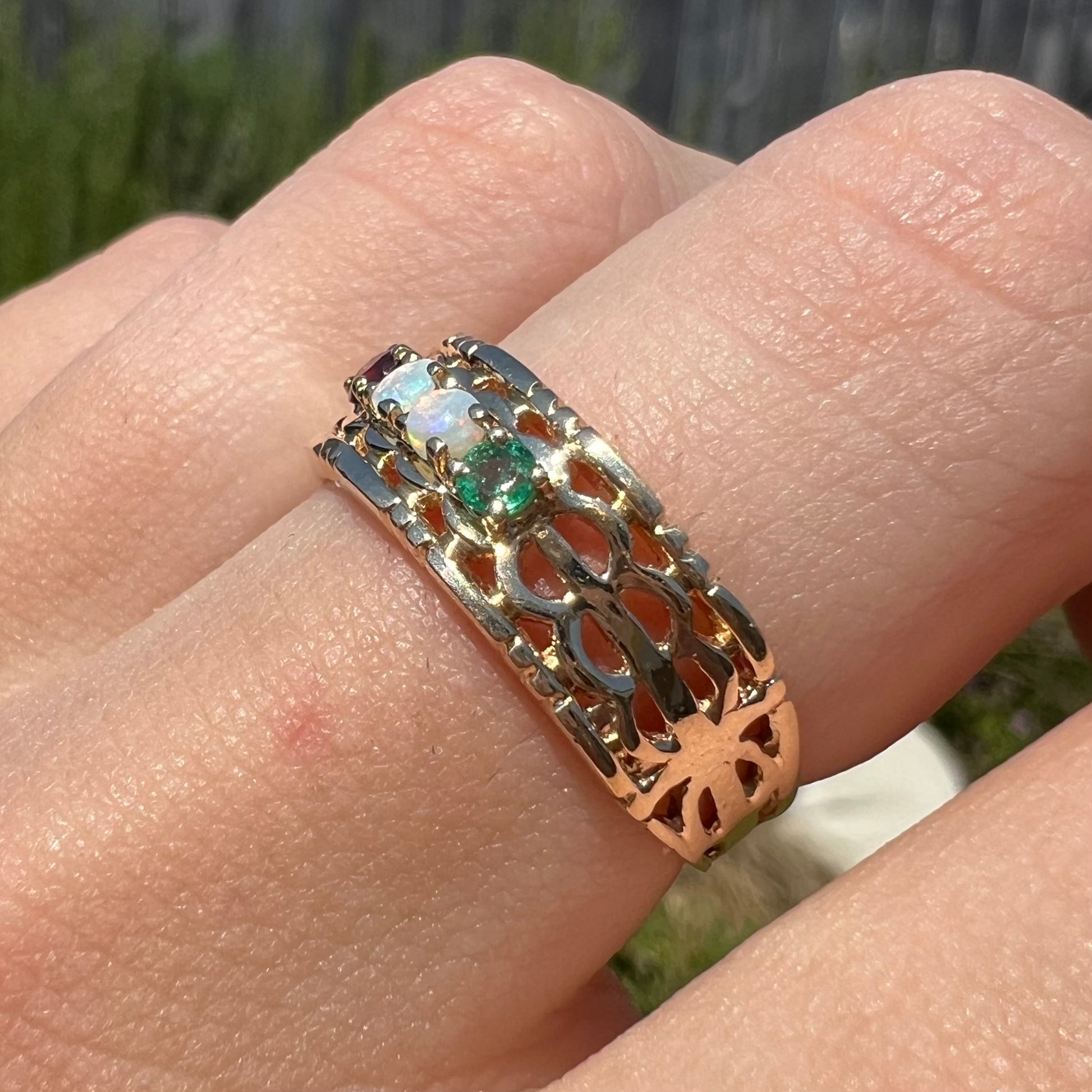 Angled sunlit view of a gold opal and emerald mother's ring.