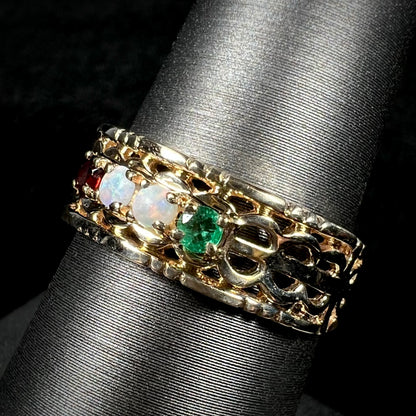 Angled view of a gold woven-style mother's ring set with two opals, an emerald, and a garnet.