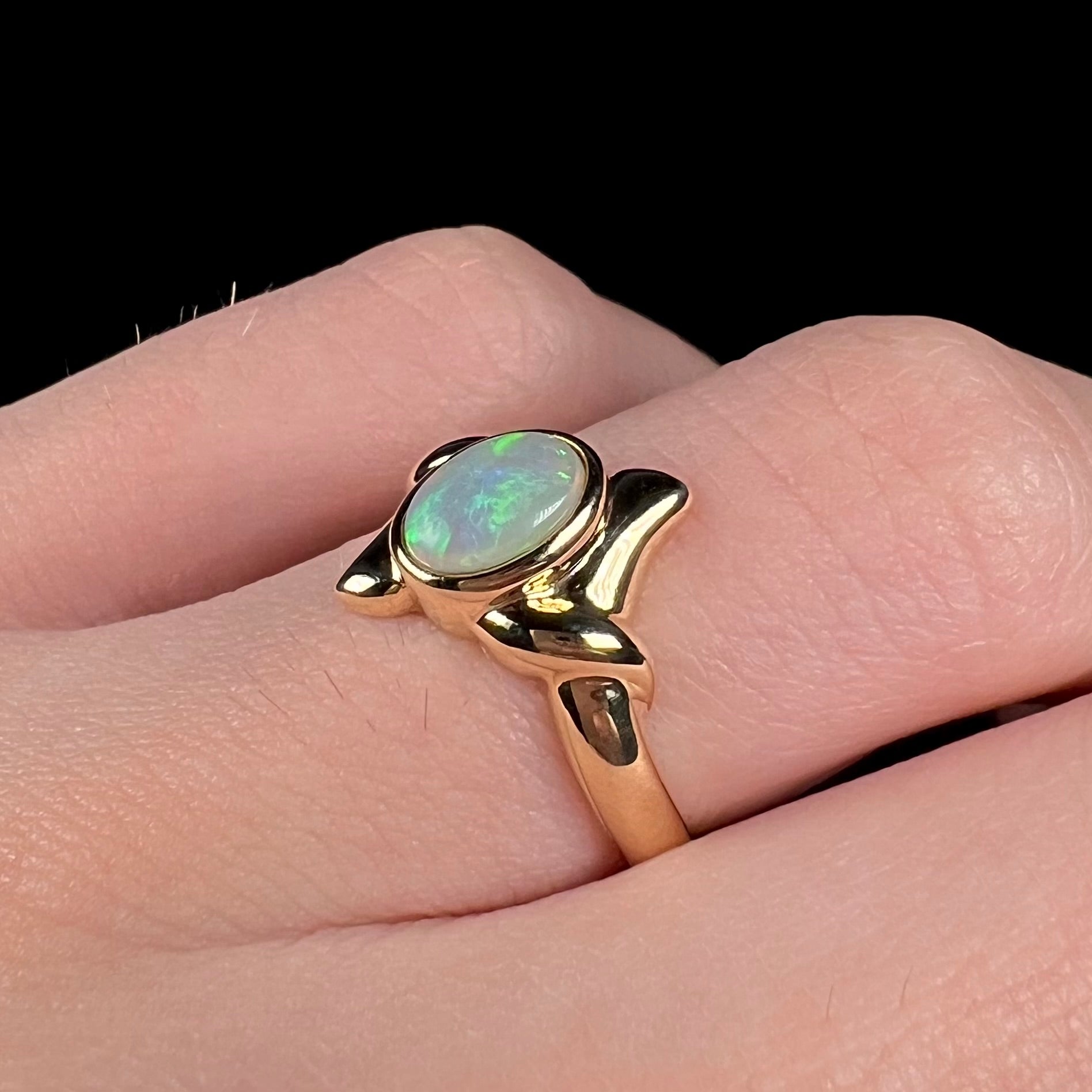 A dainty yellow gold engagement ring set with a green crystal opal, worn on a finger.