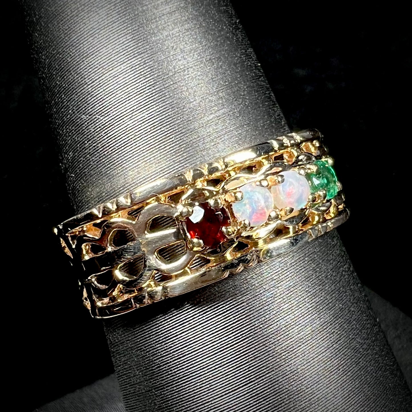 A gold woven-style mother's ring set with two opals, an emerald, and a garnet shown from an angled view.