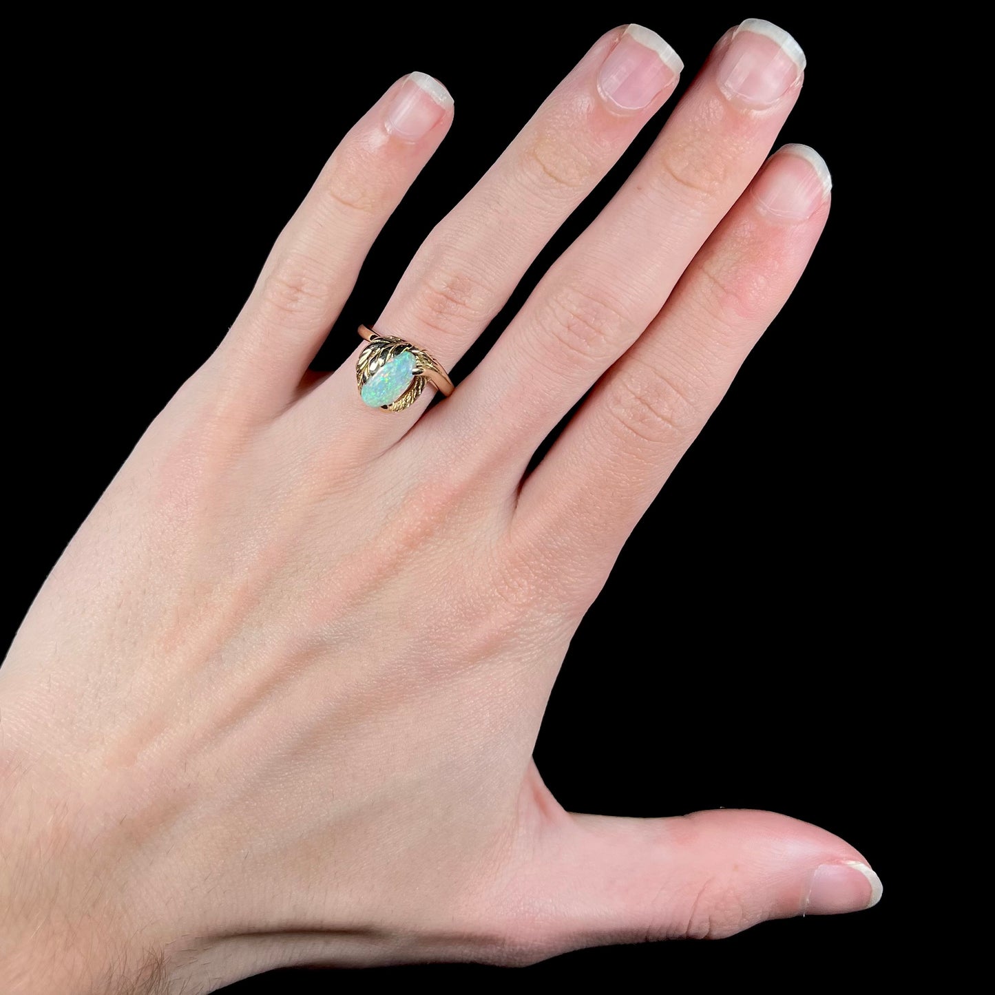 A yellow gold opal leaf-style ring worn on a hand.