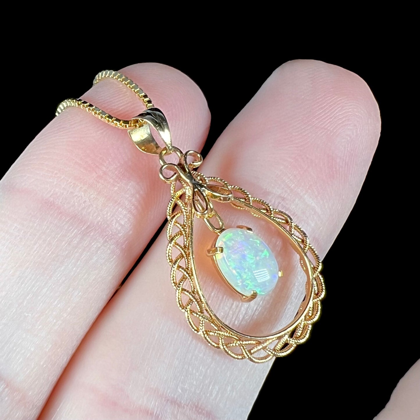 Angled macro shot of an 18k gold opal filigree necklace, with the opal appearing slightly bluish.