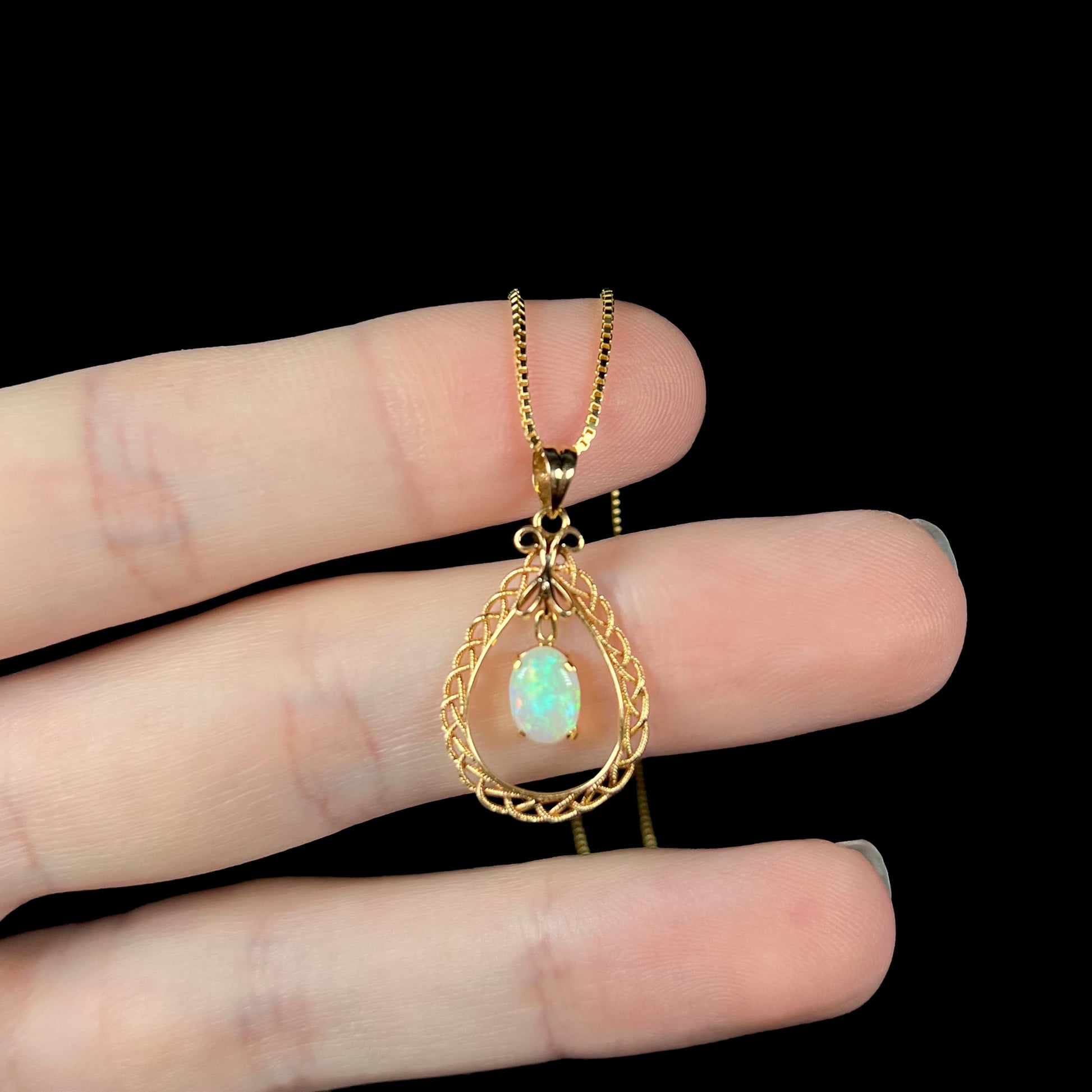 An 18k gold opal necklace resting on fingers against a black background, with subtle green flashes.