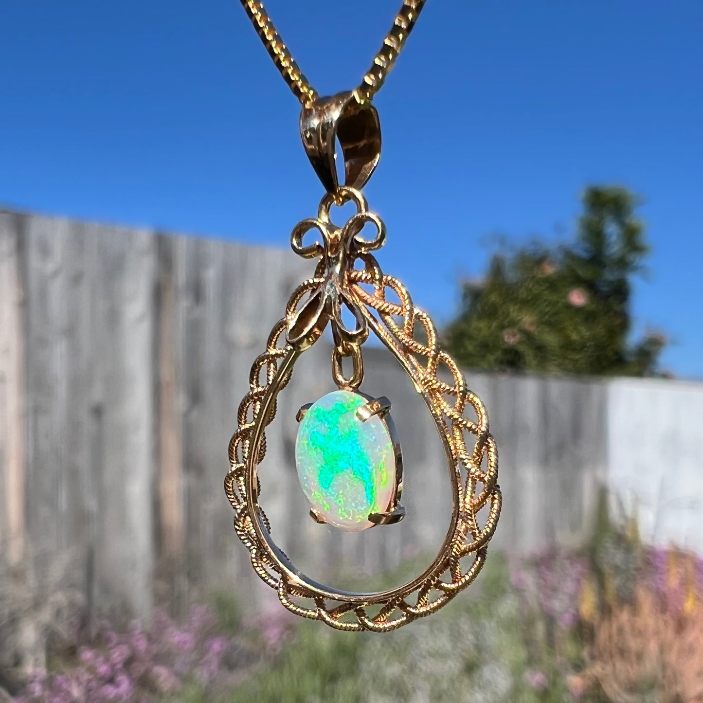 An 18k gold opal necklace outdoors, angled to reveal a vivid blue-green flash across the opal.