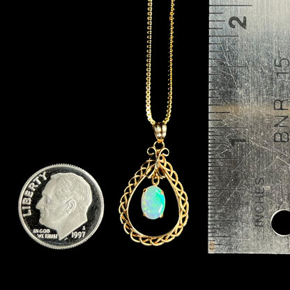 An 18k gold opal necklace placed next to a dime and ruler for scale, measuring approximately 1 inch.