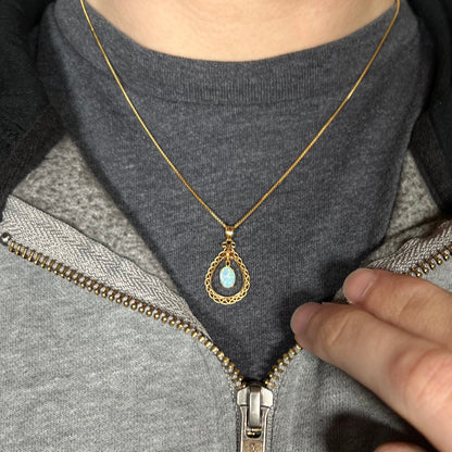 An 18k gold opal necklace worn on a black t-shirt with a partially zipped sweatshirt.