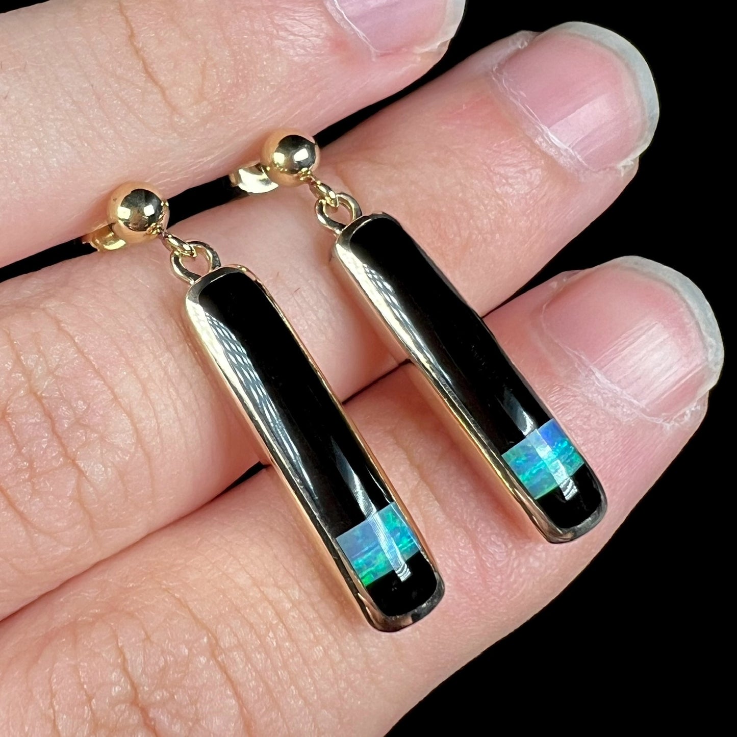 Close-up angled view of gold opal and onyx inlay dangle earrings.