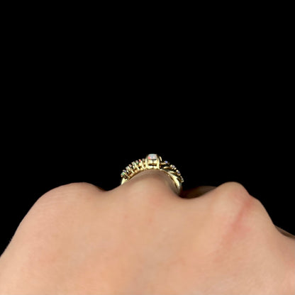 Side gallery view of a yellow gold opal crisscross ring worn on a hand, shown against a black background.
