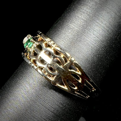 Side view of a woven-style gold band with an emerald visible.