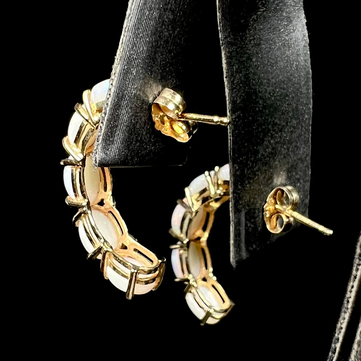 Back side of 14k gold opal semi-hoop earrings on earring display; the push-back posts and butterfly friction backs are in focus