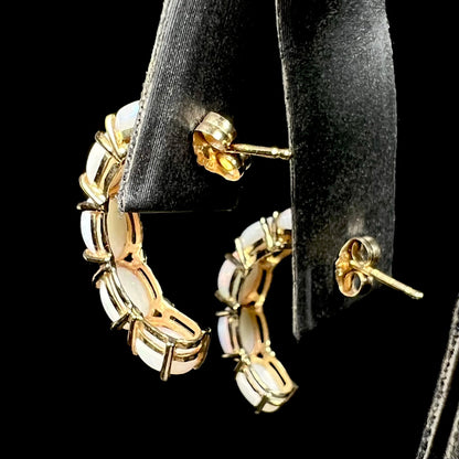 Back side of 14k gold opal semi-hoop earrings on earring display; the push-back posts and butterfly friction backs are in focus