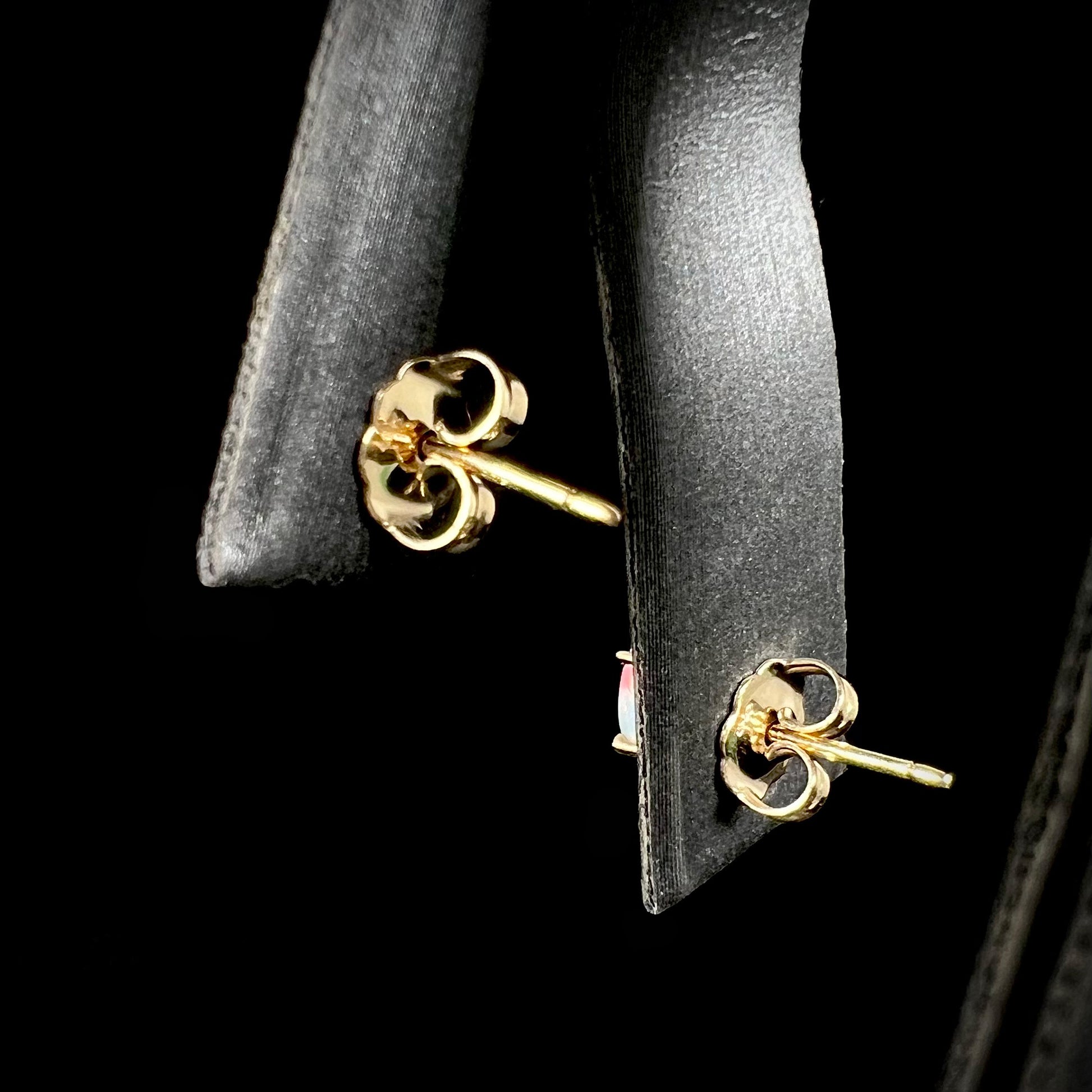 The back of opal stud earrings, showing 14k gold posts and backs against a black background.