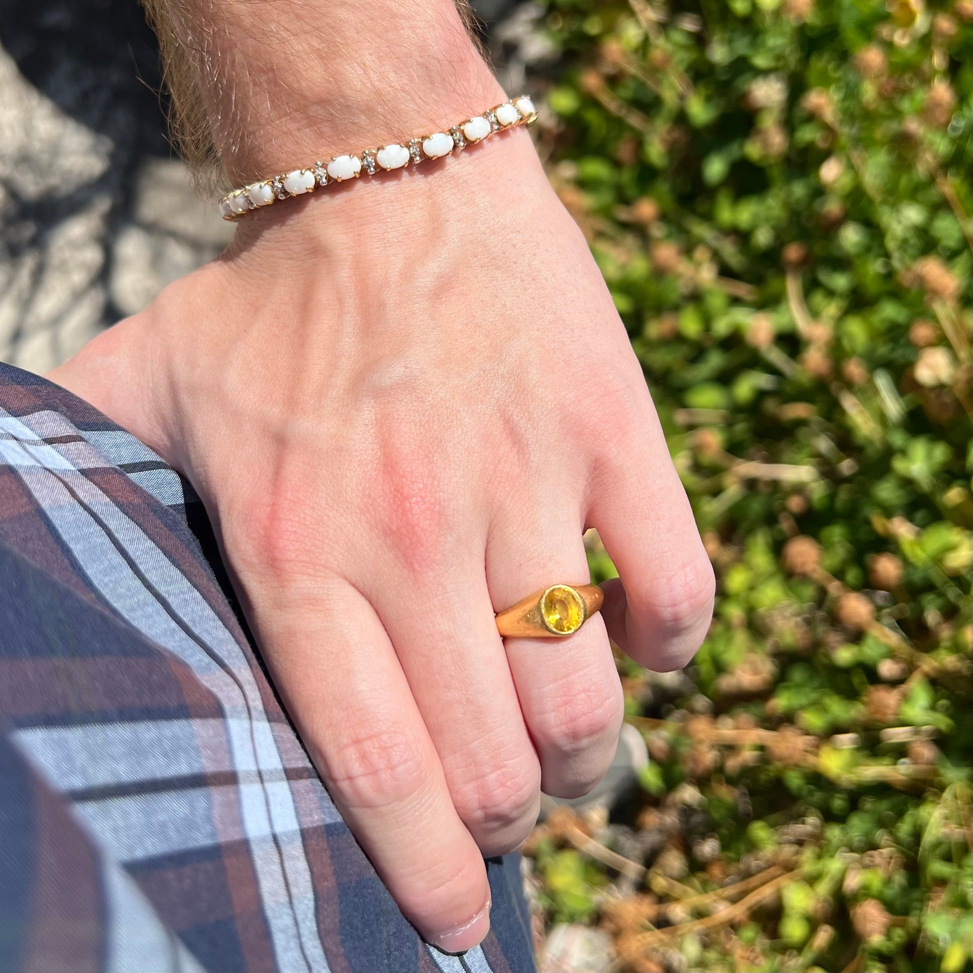 Hand resting on person's hip in sunlight while wearing a gold opal tennis bracelet on wrist with gold yellow sapphire ring on finger.