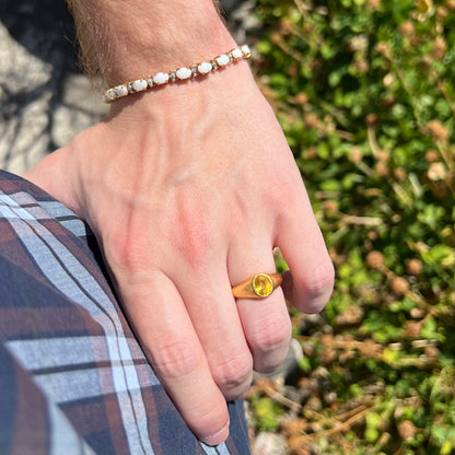 Hand resting on person's hip in sunlight while wearing a gold opal tennis bracelet on wrist with gold yellow sapphire ring on finger.