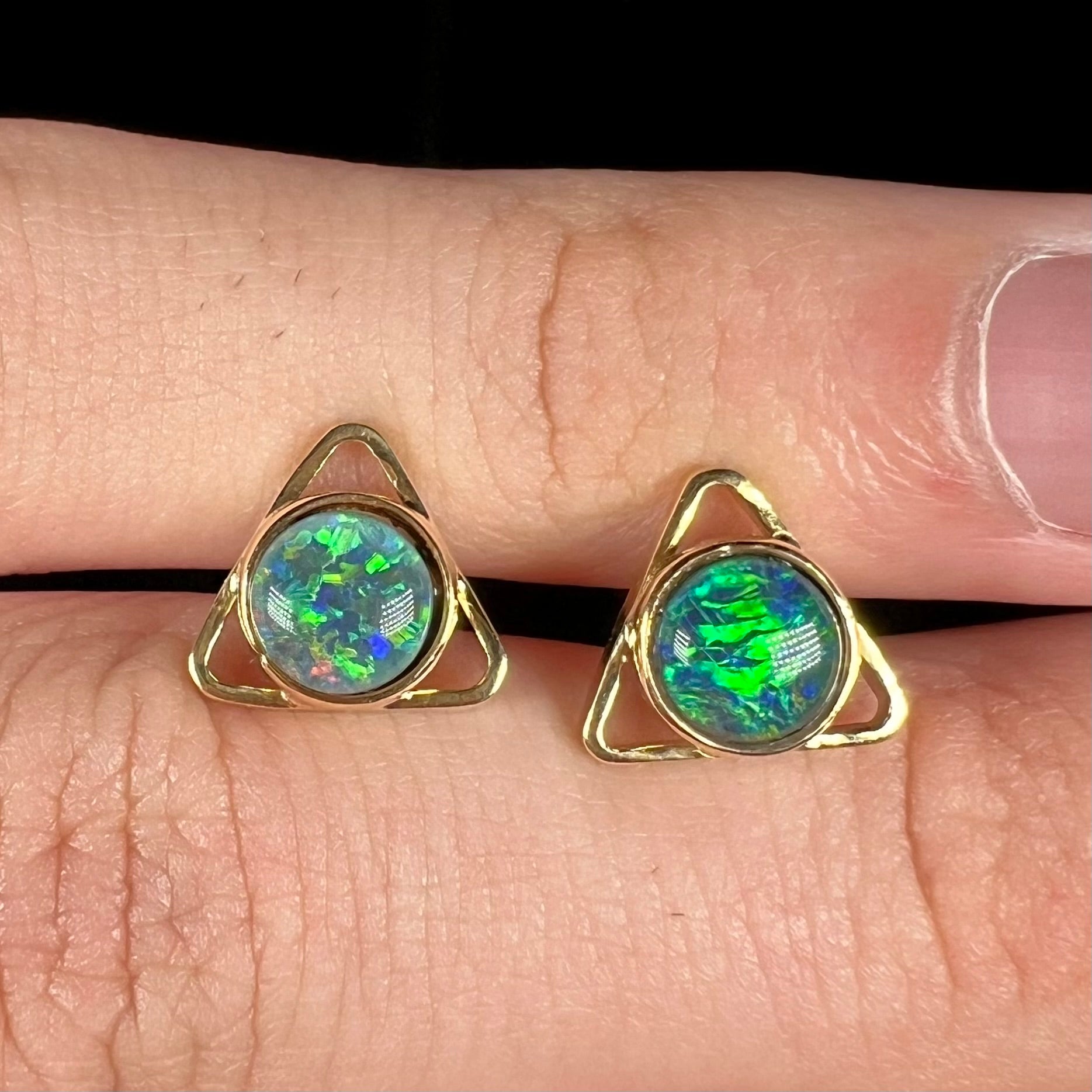 Two gold opal triplet earrings featuring an open triangle design, shown close-up on top of a hand from the front.