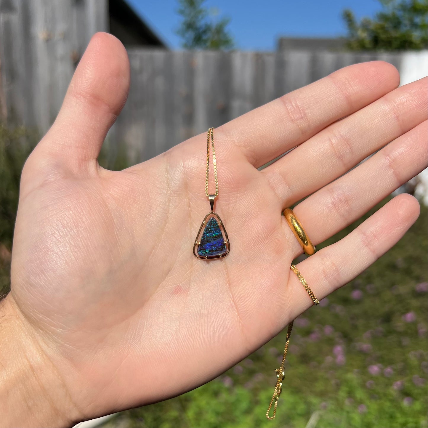 A dainty Duck Creek opalized wood necklace in 9k gold shown in the sunlight in a hand.