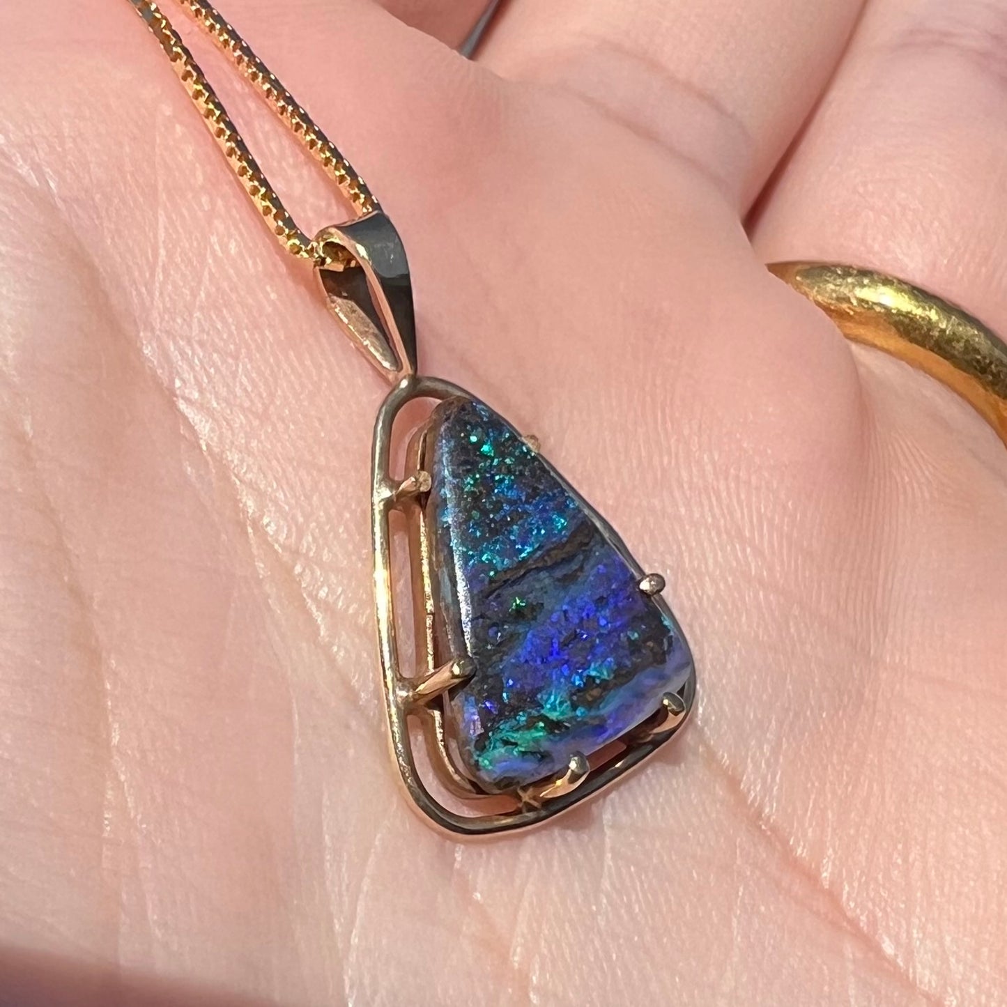 Angled close-up of a dainty Duck Creek opalized wood pendant in 9k gold, shown in a hand in sunlight.