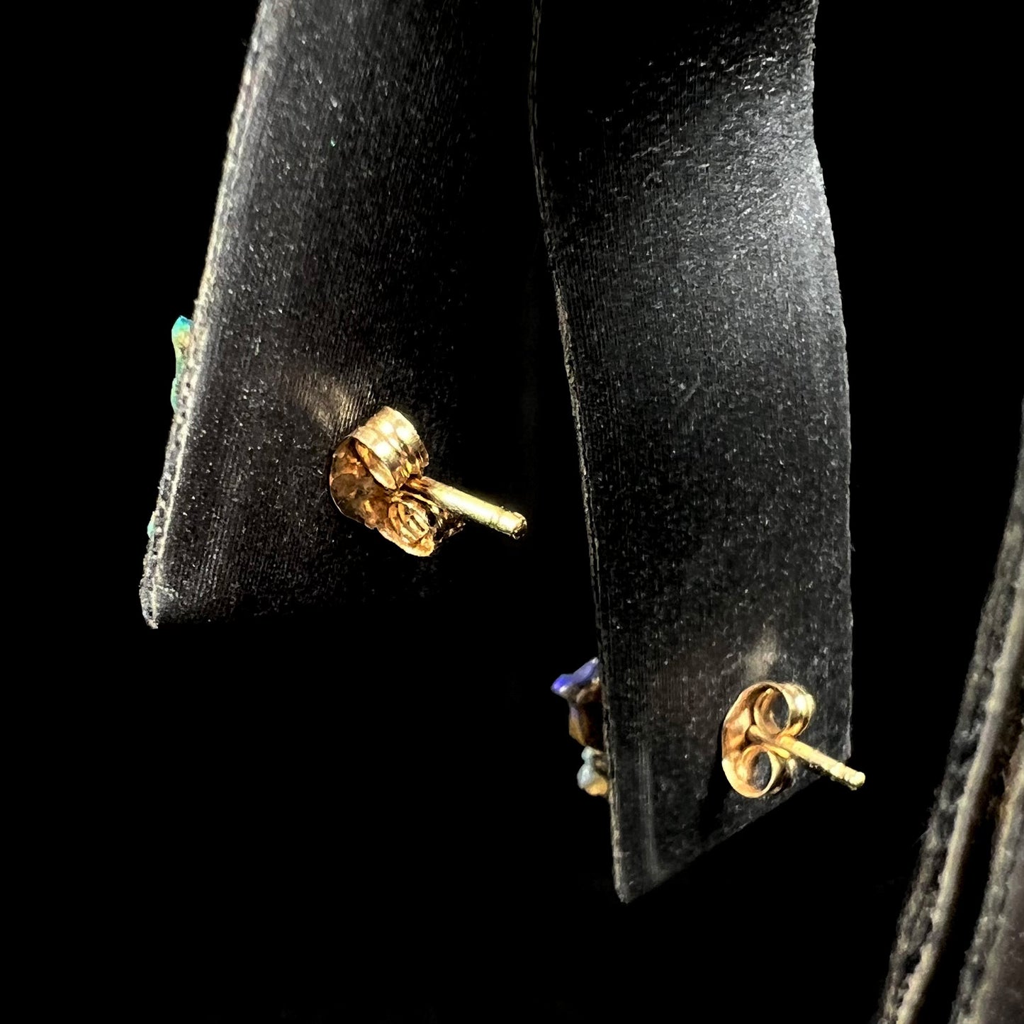Back view of gold push back earrings on an earring display against a black background.