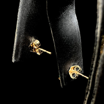 Back side of a pair of yellow gold pushback stud earrings on an earring display.
