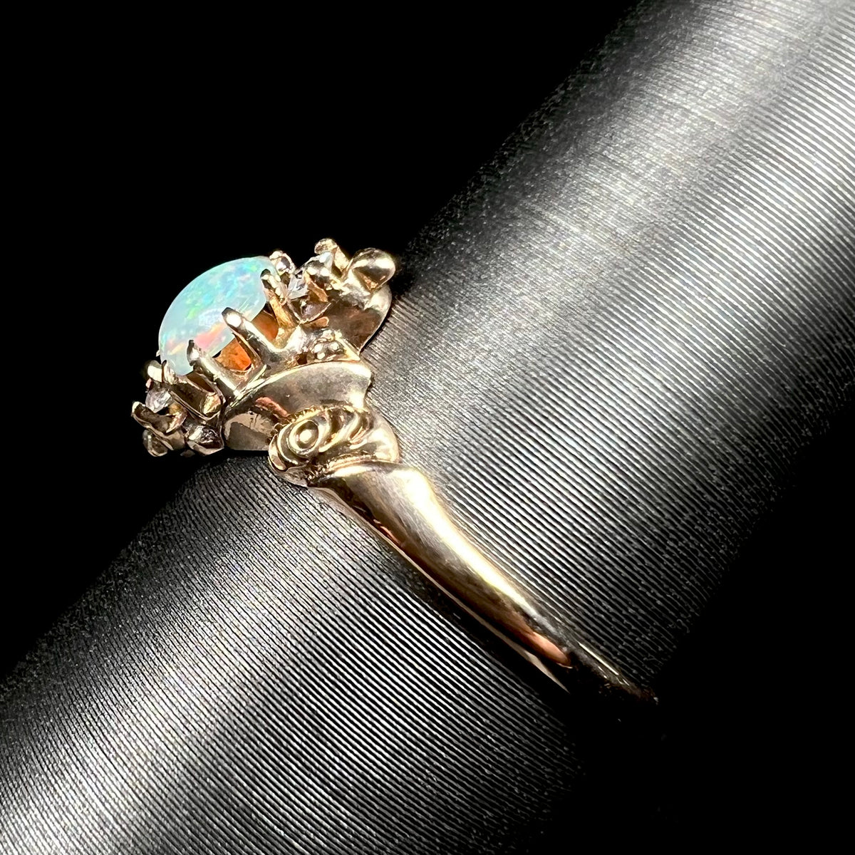 Side shank view of a yellow gold rose design opal and diamond ring, shown on ring display