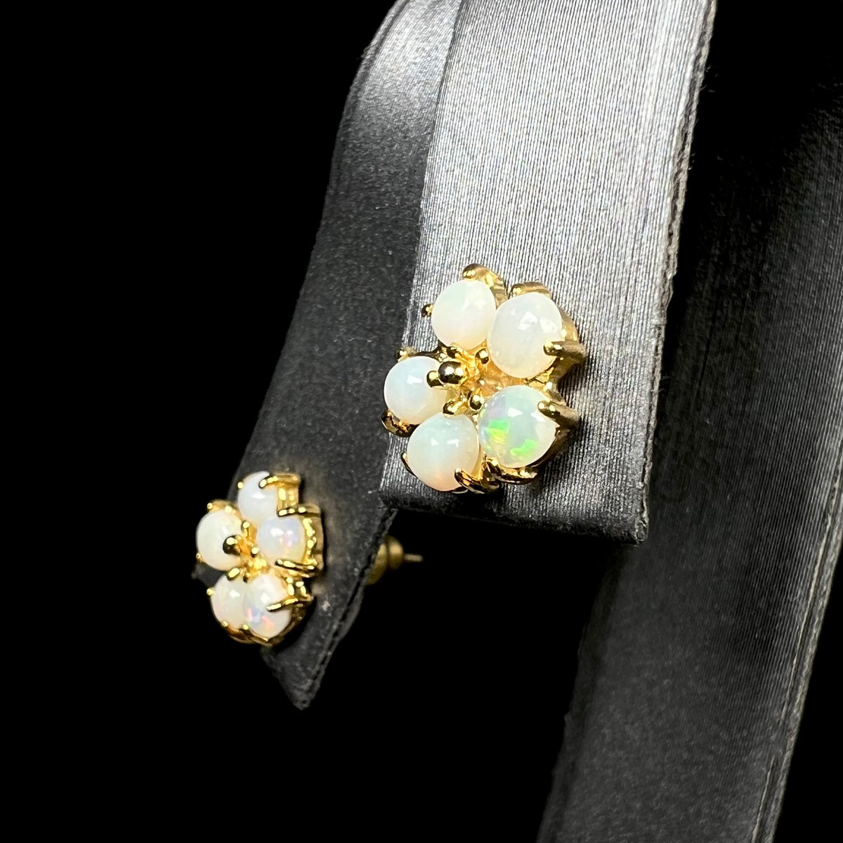 Pair of gold plated natural opal stud earrings shaped like flowers on earring display