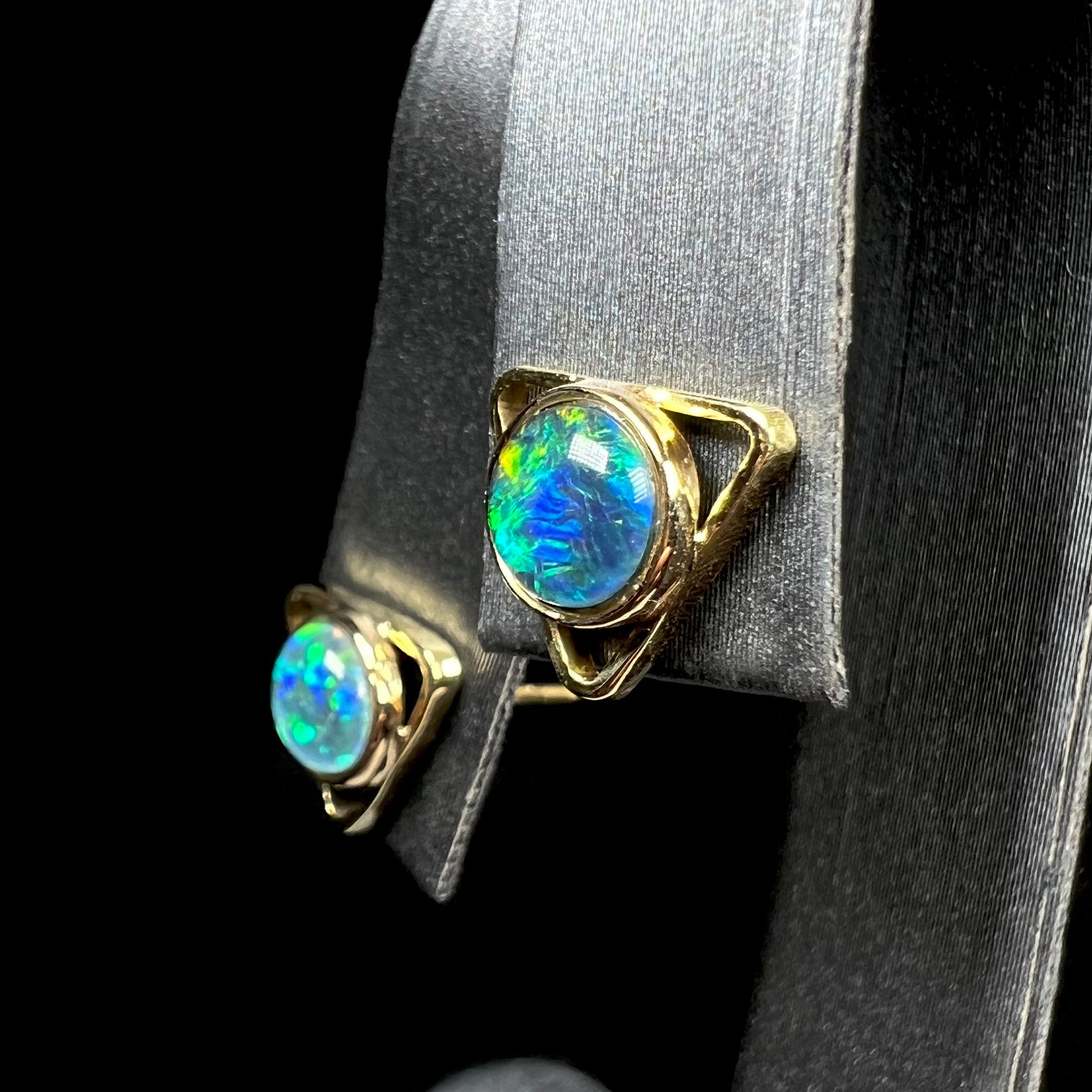 A pair of gold triangle stud earrings set with round opal triplets, shown at an angle.
