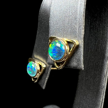 A pair of gold triangle stud earrings set with round opal triplets, shown at an angle.