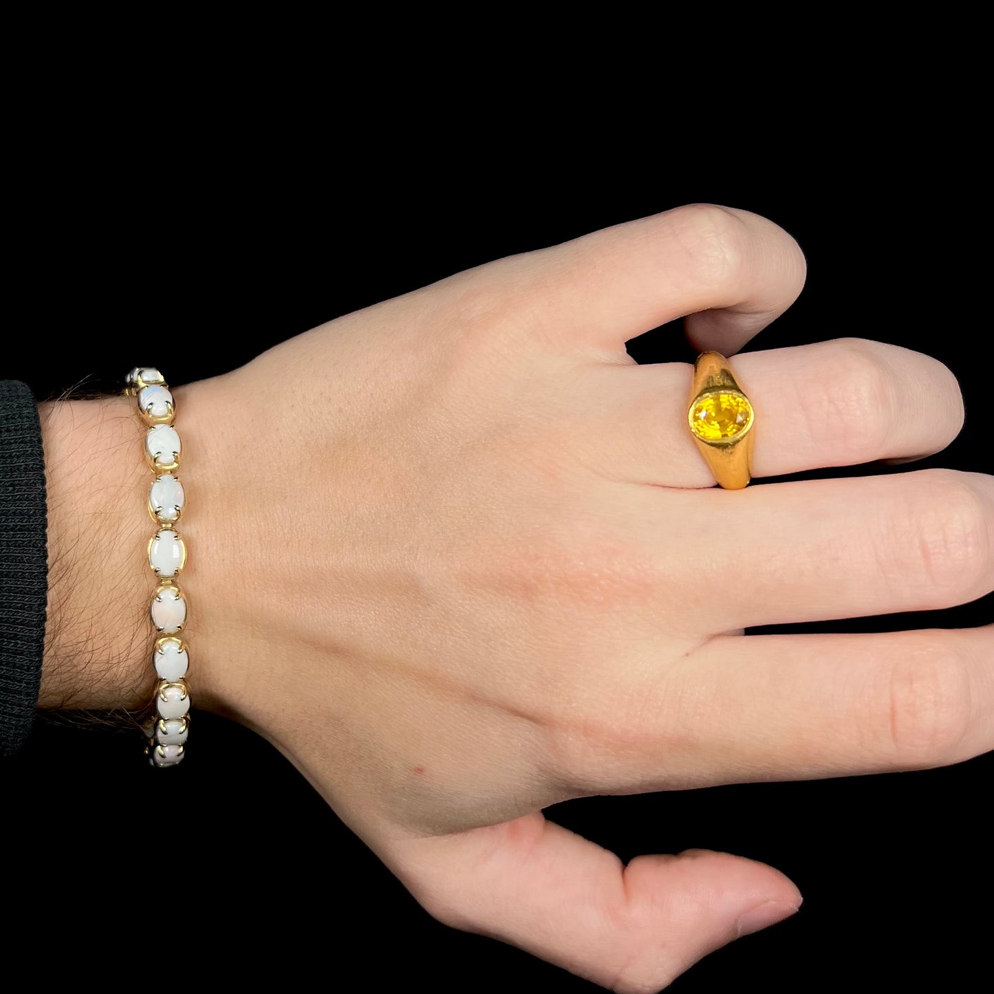 Hand wearing gold ring with women's Australian opal tennis bracelet around wrist.