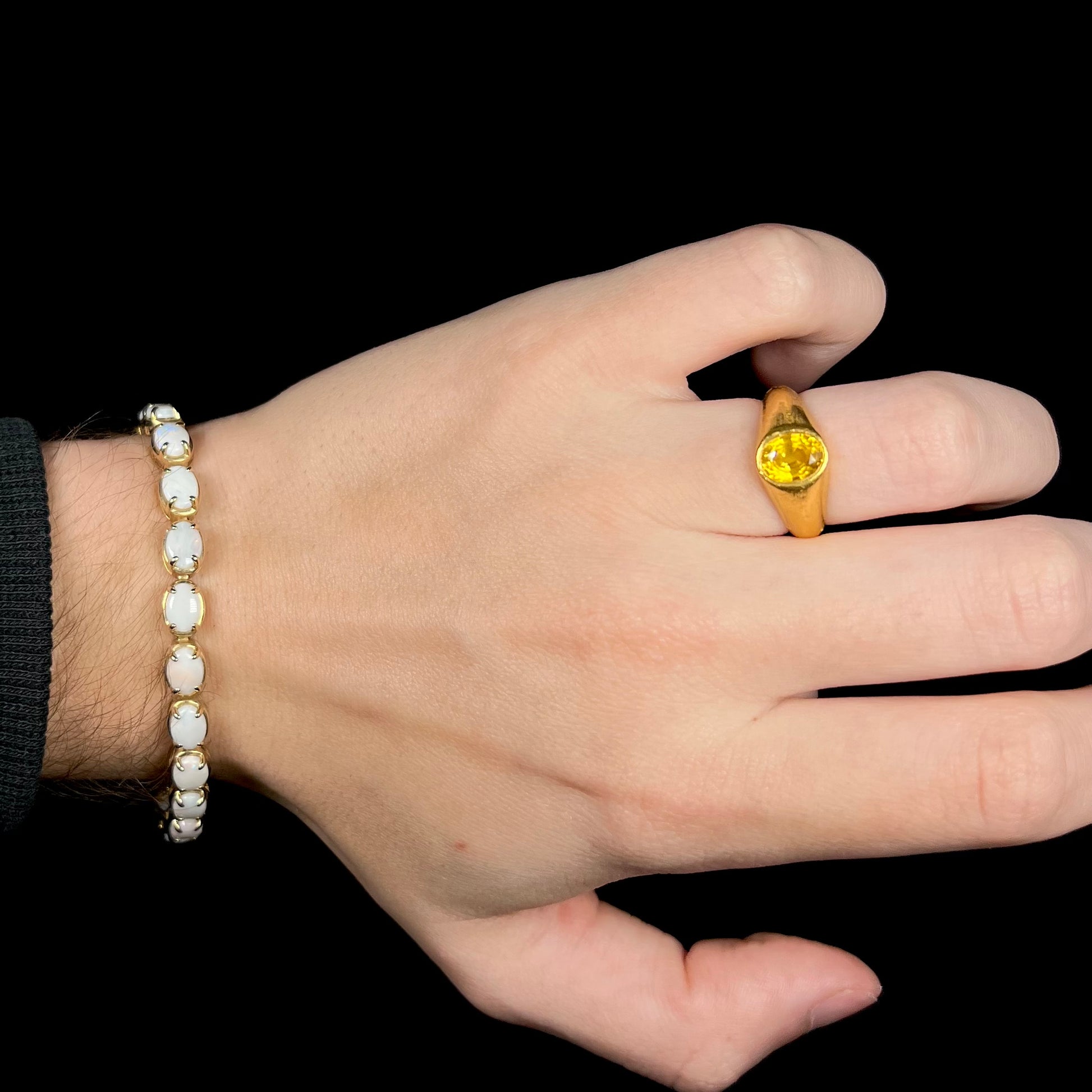 Hand wearing gold ring with women's Australian opal tennis bracelet around wrist.