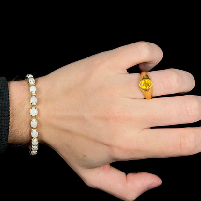 Hand wearing gold ring with women's Australian opal tennis bracelet around wrist.