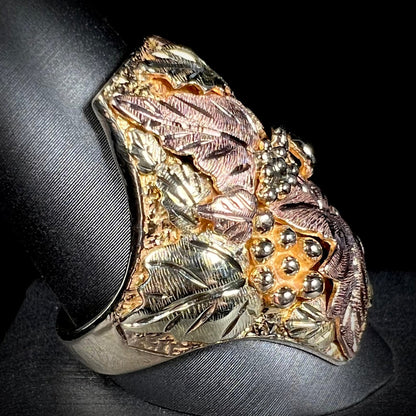 A men's solid gold ring.  The ring is Black Hills gold featuring a grapevine and leaf motif with rose and green gold designs.