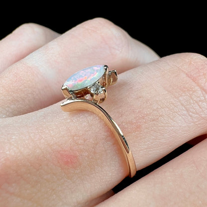 A yellow gold marquise cut opal ring set with two white sapphire accent stones.