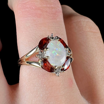 A ladies natural opal ring in yellow gold.  The opal is surrounded by red marquise cut garnets and diamonds.