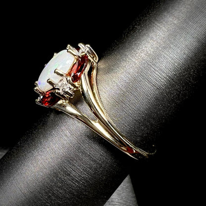 A ladies natural opal ring in yellow gold.  The opal is surrounded by red marquise cut garnets and diamonds.
