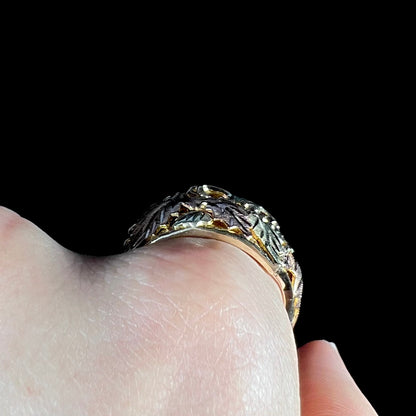 A men's solid gold ring.  The ring is Black Hills gold featuring a grapevine and leaf motif with rose and green gold designs.