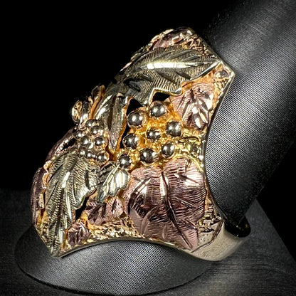 A men's solid gold ring.  The ring is Black Hills gold featuring a grapevine and leaf motif with rose and green gold designs.