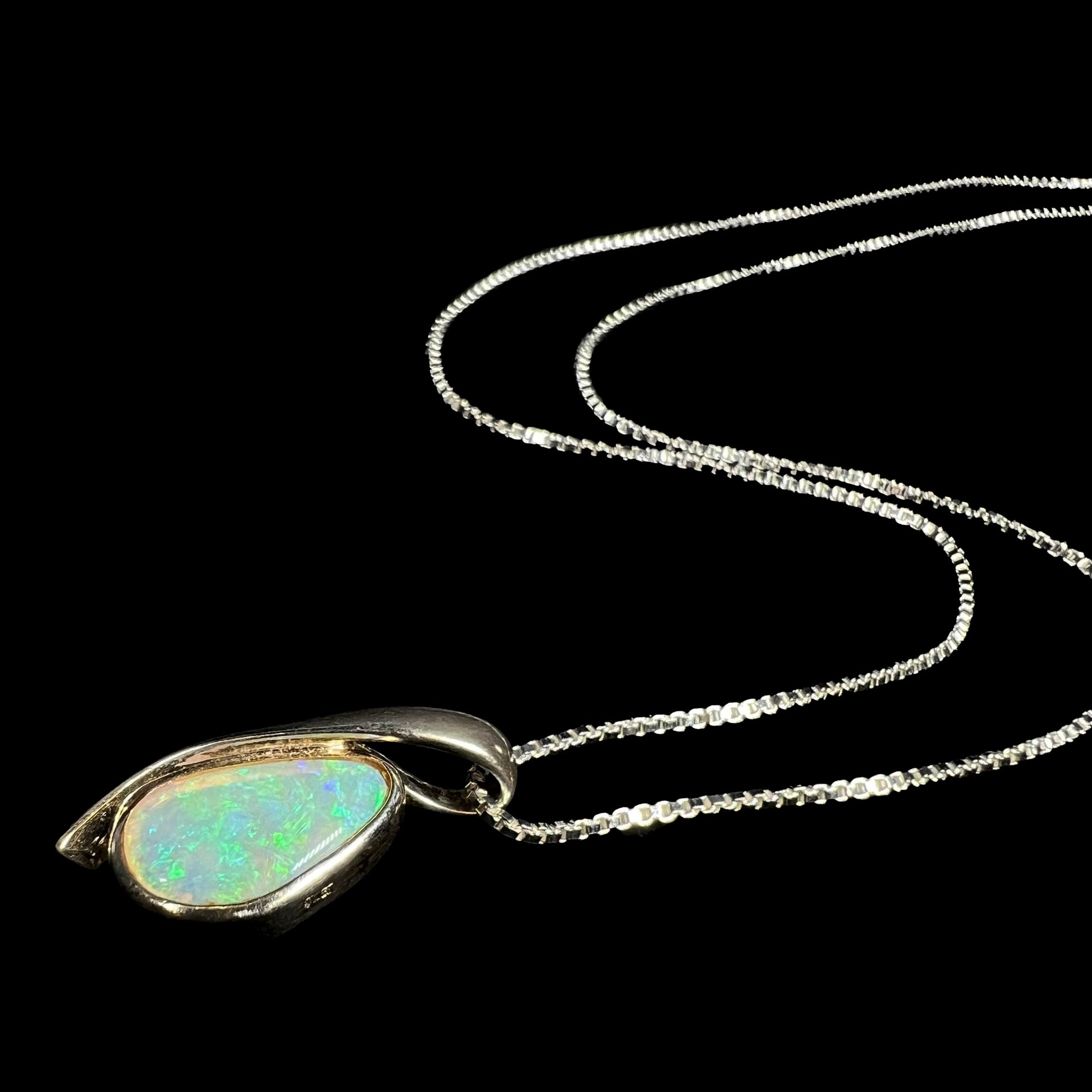 A green Australian crystal opal necklace in sterling silver shown from an angle as it lays against a black background.