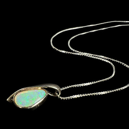 A green Australian crystal opal necklace in sterling silver shown from an angle as it lays against a black background.