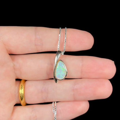 A green Australian crystal opal necklace in sterling silver shown held in a hand against a black background.