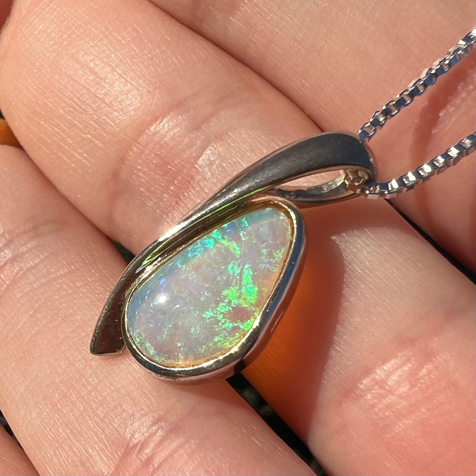 A green Australian crystal opal pendant in sterling silver shown close-up in a hand from an angle in the sunlight.