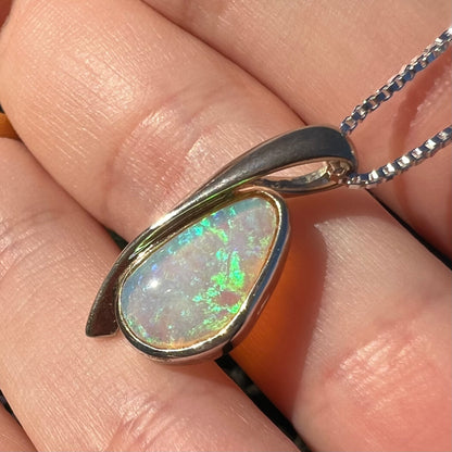 A green Australian crystal opal pendant in sterling silver shown close-up in a hand from an angle in the sunlight.