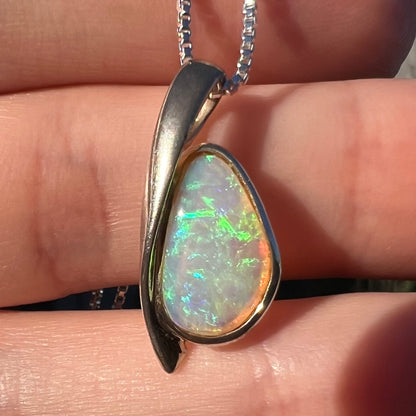 Close-up of a green Australian crystal opal pendant in sterling silver shown in a hand in the sunlight.